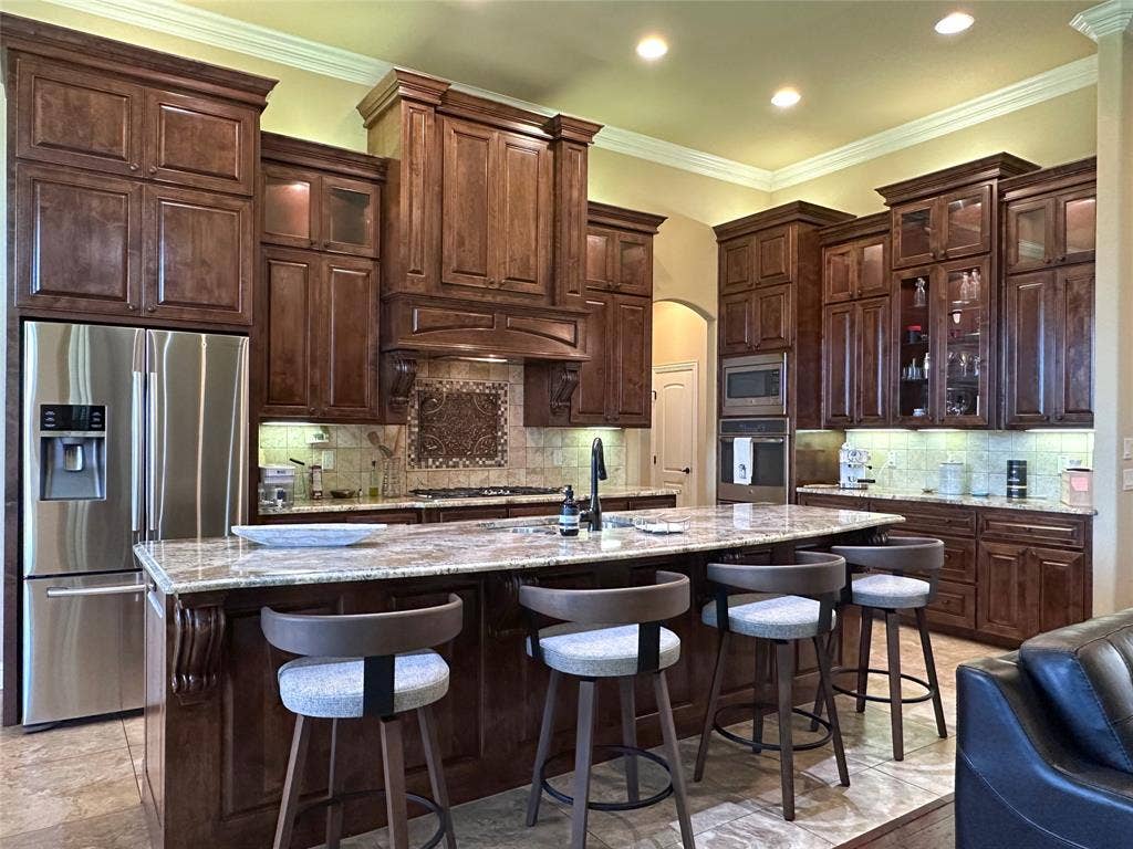 1100 Wessex Drive, Woodway, TX 76712 Kitchen featuring extensive dark wood cabinetry, a large kitchen island with counter seating, stainless steel appliances, and a decorative tile backsplash