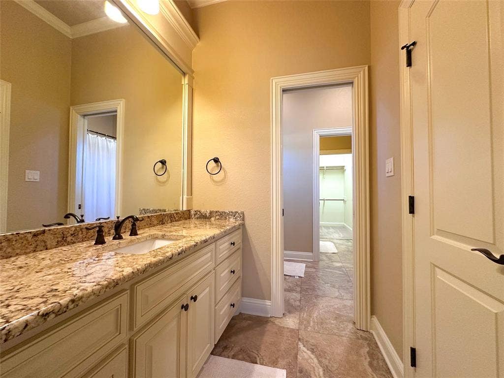 1100 Wessex Drive, Woodway, TX 76712 Bathroom vanity featuring a light-toned stone countertop, dual-basin sink, and dark bronze fixtures