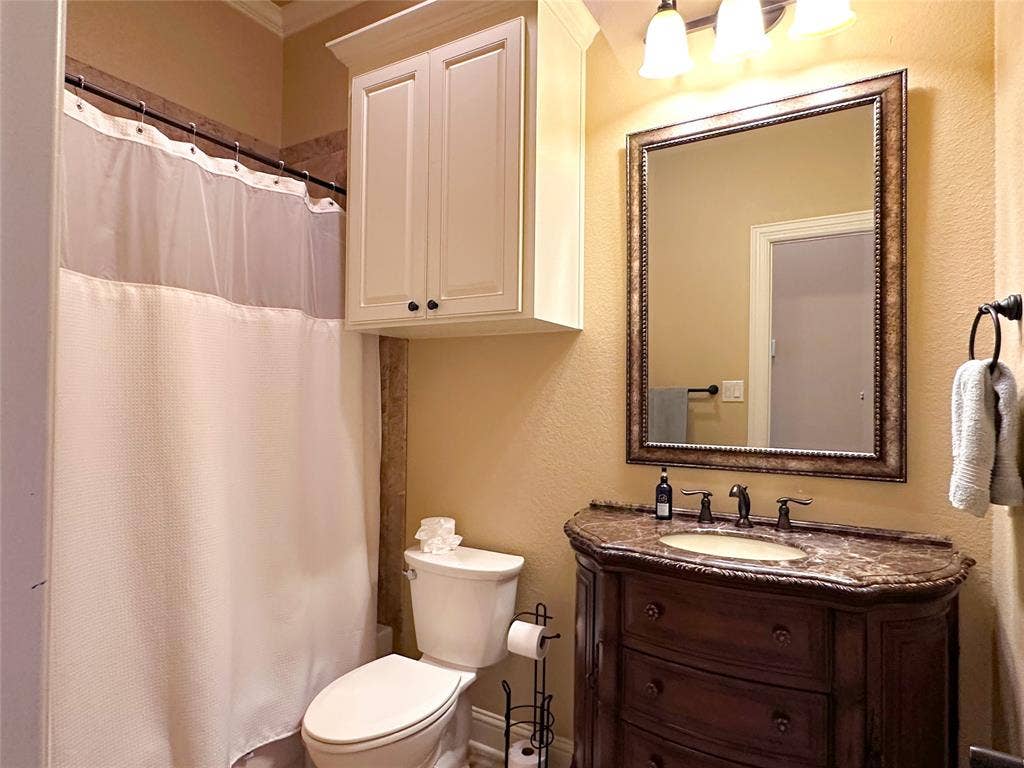 1100 Wessex Drive, Woodway, TX 76712 Bathroom featuring an ornate dark wood vanity with a stone countertop, a framed mirror, and a wall-mounted light fixture