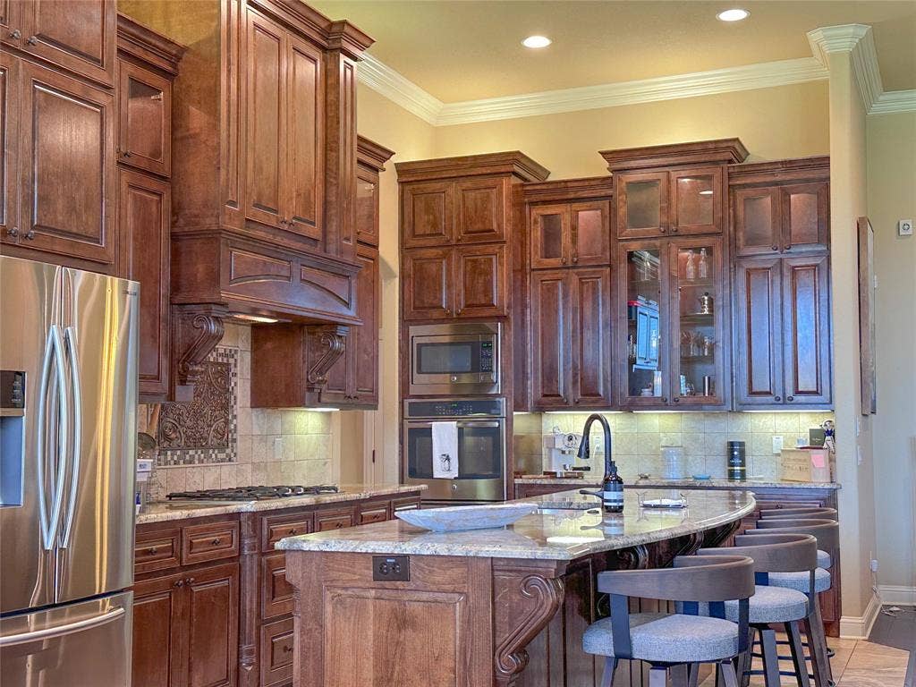 1100 Wessex Drive, Woodway, TX 76712 Gourmet kitchen featuring custom wood cabinetry with crown molding, granite countertops, stainless steel appliances, a gas cooktop, and an integrated beverage bar