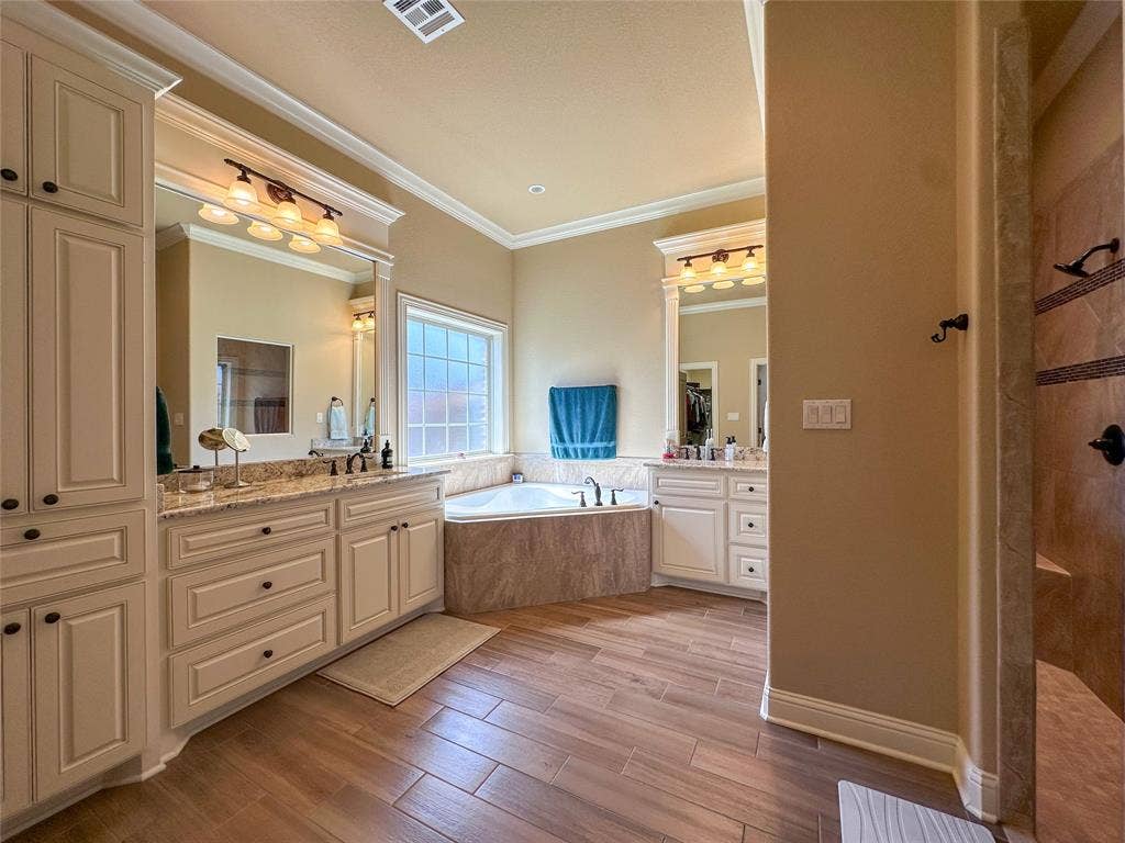 1100 Wessex Drive, Woodway, TX 76712 Bathroom featuring wood-finish flooring, a corner soaking tub with tiled surround, and dual vanities with granite countertops