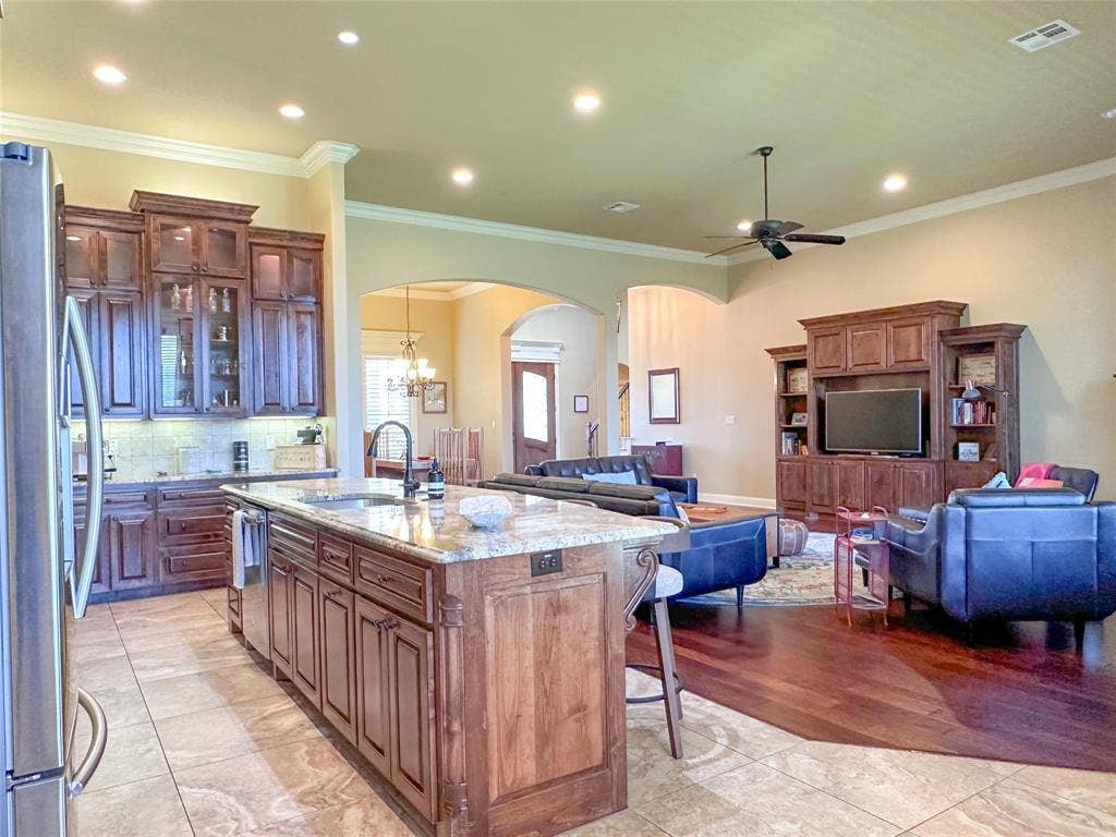 1100 Wessex Drive, Woodway, TX 76712 Expansive kitchen and living area featuring a large center island with a granite countertop, dark wood-finish cabinetry, recessed lighting, and a built-in entertainment center