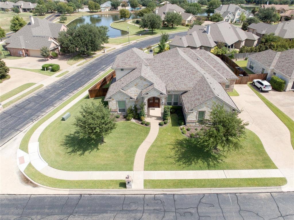 1100 Wessex Drive, Woodway, TX 76712 Stone-clad residence featuring a curved entry walkway, mature landscaping, a multi-gabled roofline, and an expansive driveway