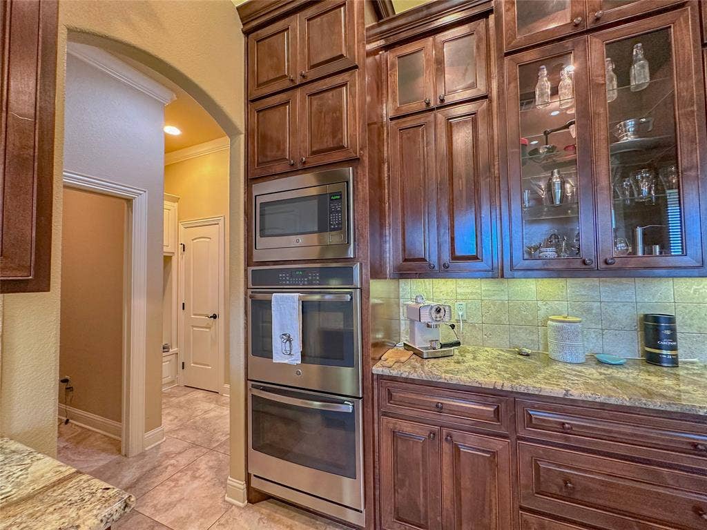 1100 Wessex Drive, Woodway, TX 76712 Kitchen featuring wood-finish cabinetry, stainless steel built-in microwave and oven, stone countertops, and tile backsplash