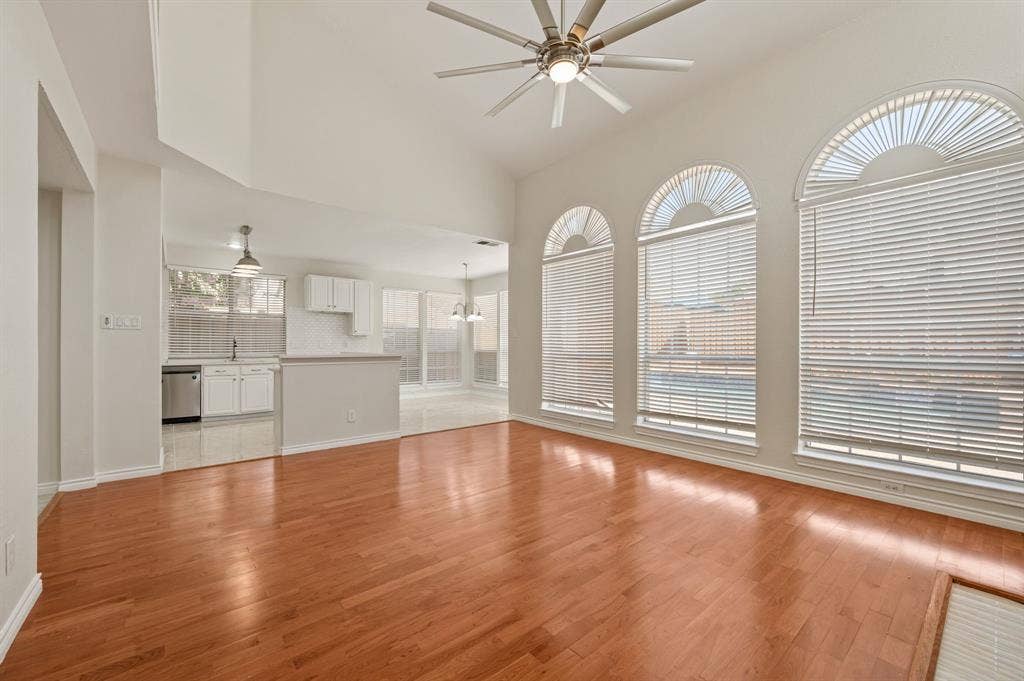 669 Water Oak Drive, Plano, TX 75025 Spacious living area featuring high vaulted ceilings with a ceiling fan, lustrous wood-finish flooring, and a bank of three large arched windows with blinds