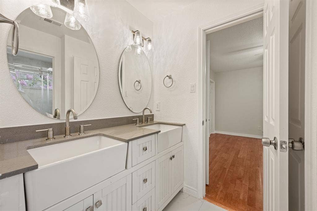 669 Water Oak Drive, Plano, TX 75025 Double vanity featuring two farmhouse sinks, gray countertops, brushed nickel fixtures, and individual circular mirrors