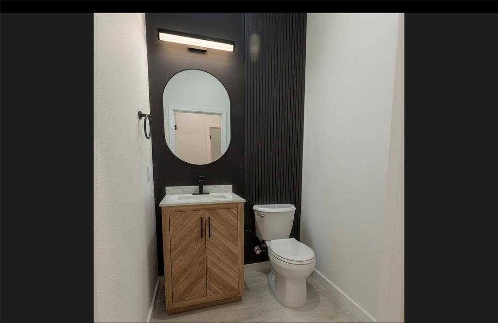 3315 Kyser, Dallas, TX 75216 Modern powder room featuring a wood-finish vanity with chevron doors, a countertop, an oval-shaped mirror, and a sleek wall-mounted light fixture