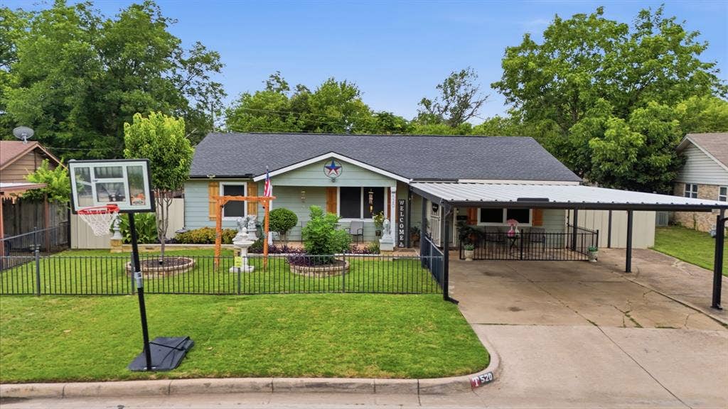 520 Thompson Drive, Saginaw, TX 76179 Light blue siding facade with dark roof, featuring a covered carport, wrought iron fencing, and mature landscaping