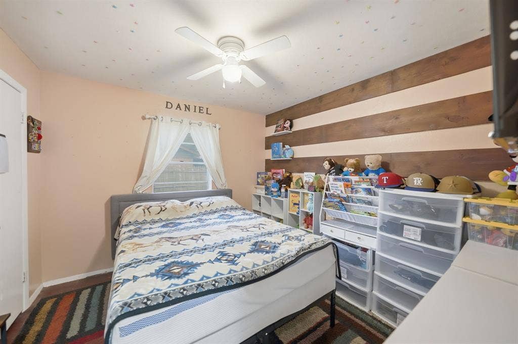 520 Thompson Drive, Saginaw, TX 76179 Bedroom featuring a wood-finish accent wall, light-colored walls, ceiling fan with integrated lighting, and a window with sheer curtains