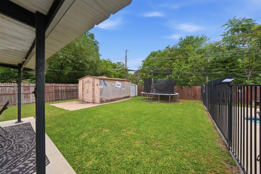 520 Thompson Drive, Saginaw, TX 76179 Expansive green lawn featuring a detached storage shed on a concrete pad, a black metal fence, and a wooden privacy fence