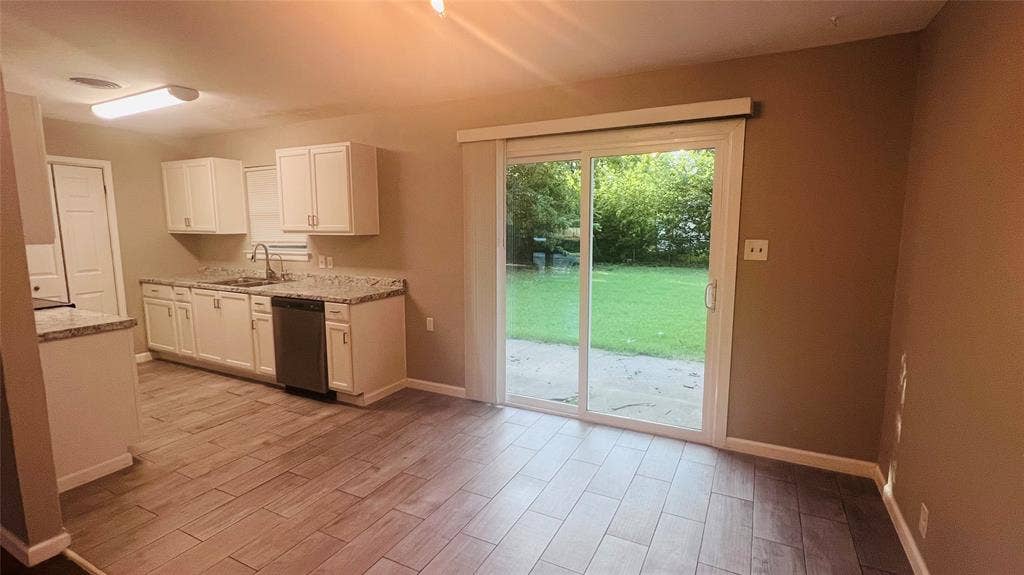 909 Laguna Drive, Denton, TX 76209 Open-concept kitchen and dining area featuring wood-finish flooring, white cabinetry, a stainless steel dishwasher, and a sliding glass door leading to a patio and grassy yard