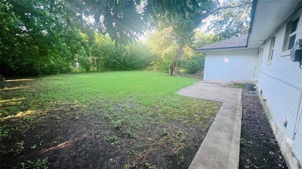 909 Laguna Drive, Denton, TX 76209 Expansive rear yard featuring a large grass area, mature trees, concrete patio, and a concrete pathway along the residence