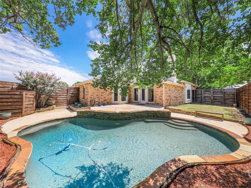 6701 Vero Drive, Plano, TX 75023 Backyard oasis featuring a curvilinear swimming pool with integrated steps, stone coping, and a surrounding concrete patio. Note the pool equipment is located at the back of the lot near the driveway and garage behind a board on board fence to protect and hide the equipment.