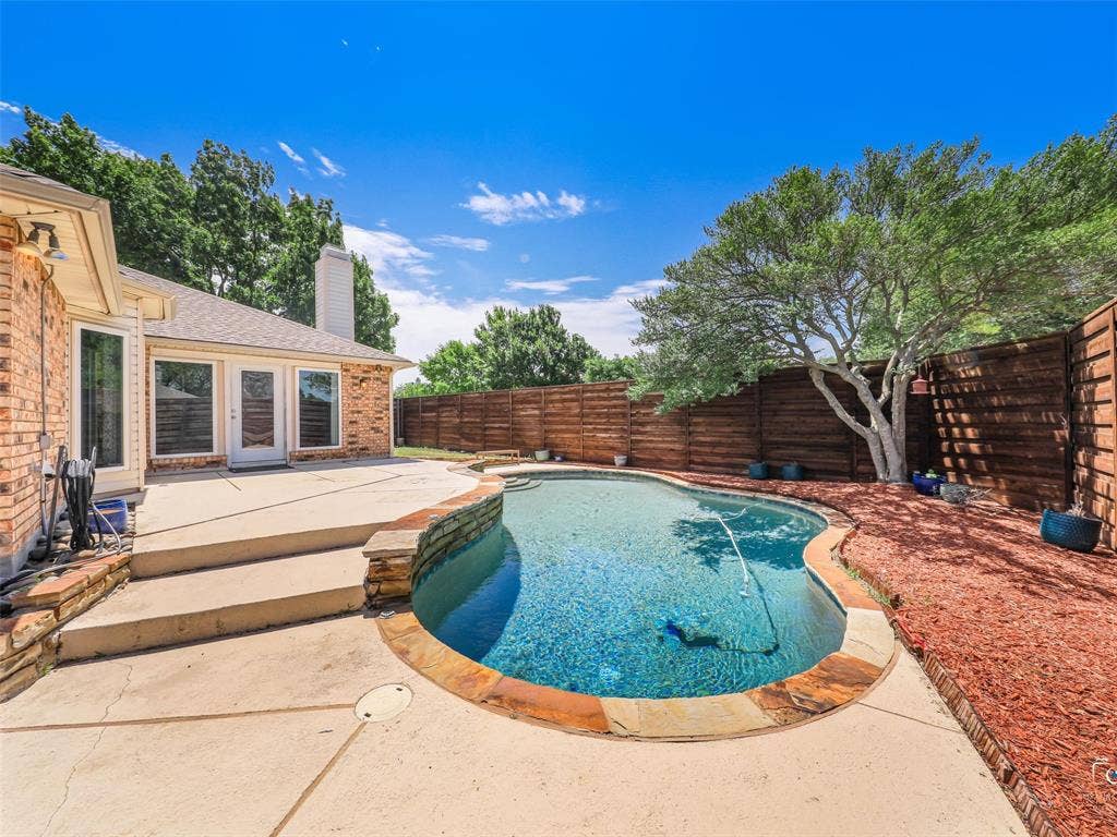 6701 Vero Drive, Plano, TX 75023 Backyard swimming pool with stone coping and an expansive concrete patio and a view of the back of the home.