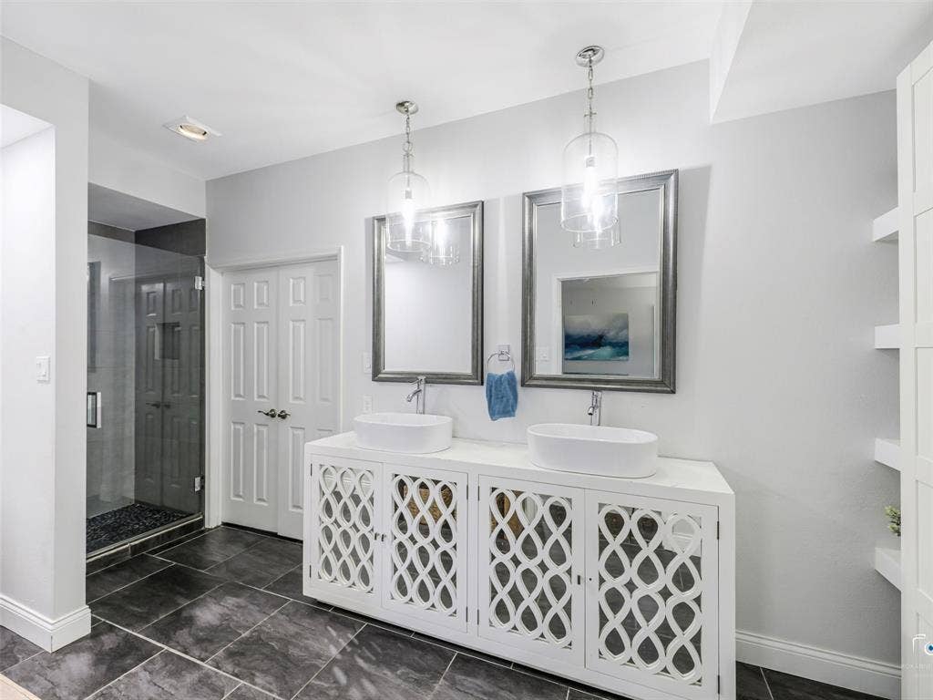6701 Vero Drive, Plano, TX 75023 Contemporary bathroom featuring a double vanity with vessel sinks and decorative cabinet fronts, tile floors and a large walk-in shower. The spacious primary closet is beyond the double doors.