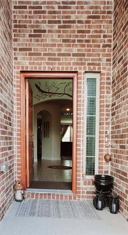 104 Rustic Oak Lane, McKinney, TX 75072 Brick exterior entrance with a solid wood door, sidelight window, and tiled interior flooring