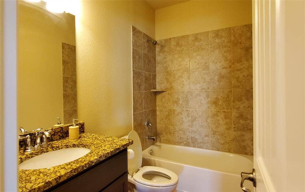 104 Rustic Oak Lane, McKinney, TX 75072 Bathroom featuring a white bathtub, ceramic tile shower surround with integrated shelf, vanity with a granite countertop, undermount sink, and chrome fixtures
