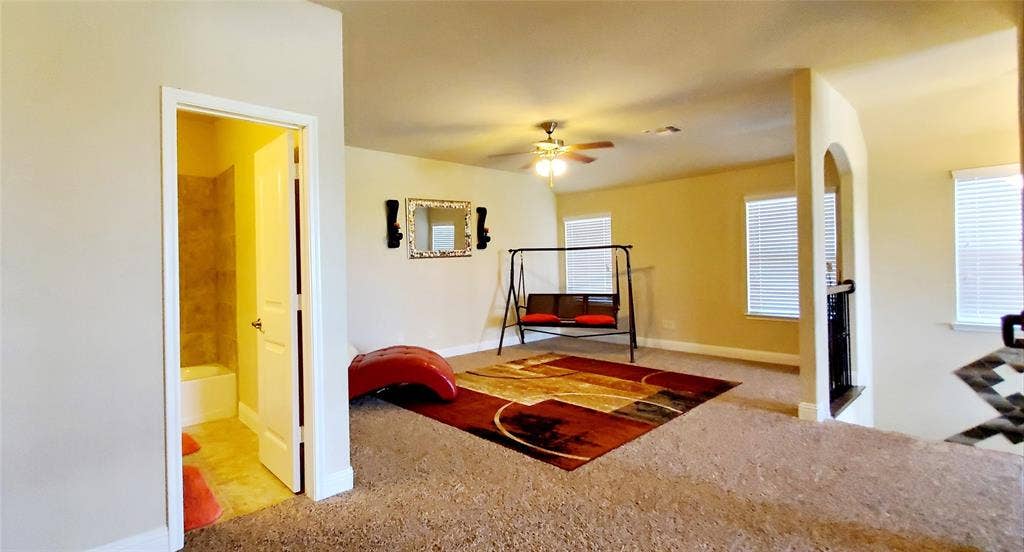 104 Rustic Oak Lane, McKinney, TX 75072 Carpeted upper-level space featuring a ceiling fan, multiple windows with blinds, an arched doorway, and an adjacent bathroom with a tub/shower combination