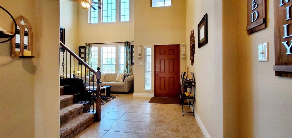 104 Rustic Oak Lane, McKinney, TX 75072 Two-story foyer featuring tile flooring, a dark wood entry door with a sidelight, and a staircase with dark wood newel posts and wrought iron balusters