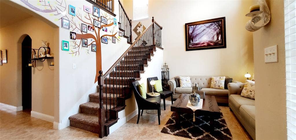 104 Rustic Oak Lane, McKinney, TX 75072 Inviting living area featuring a prominent staircase with dark wood-finish banisters and carpeted treads, alongside light-toned tile flooring