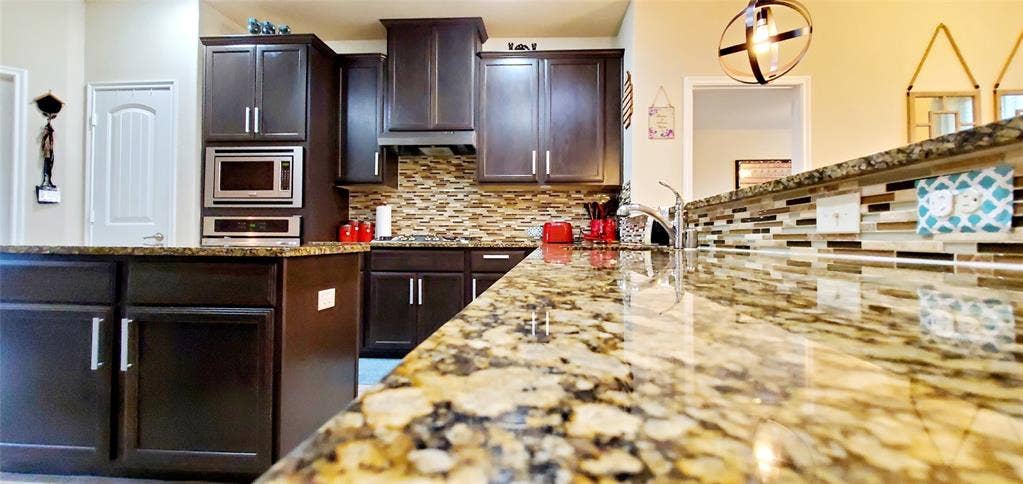 104 Rustic Oak Lane, McKinney, TX 75072 Spacious kitchen featuring expansive stone countertops, dark wood cabinetry, a mosaic tile backsplash, built-in stainless steel appliances, and a kitchen island with additional storage