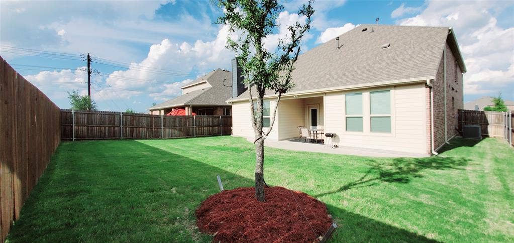 104 Rustic Oak Lane, McKinney, TX 75072 Expansive backyard featuring a manicured lawn, a young tree with mulch, and full privacy fencing