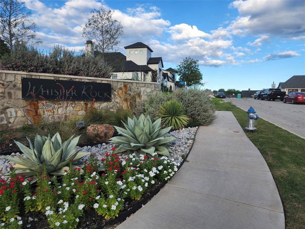 1203 Chapel Drive, Rockwall, TX 75032 Stone entry monument with integrated sign, lush landscaping featuring agaves and flowering plants, and a concrete pedestrian path