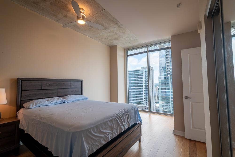 360 Nueces Street, #2110, Austin, TX 78701 Floor-to-ceiling windows with urban skyscraper backdrop, hardwood flooring, and a modern ceiling fan with integrated lighting