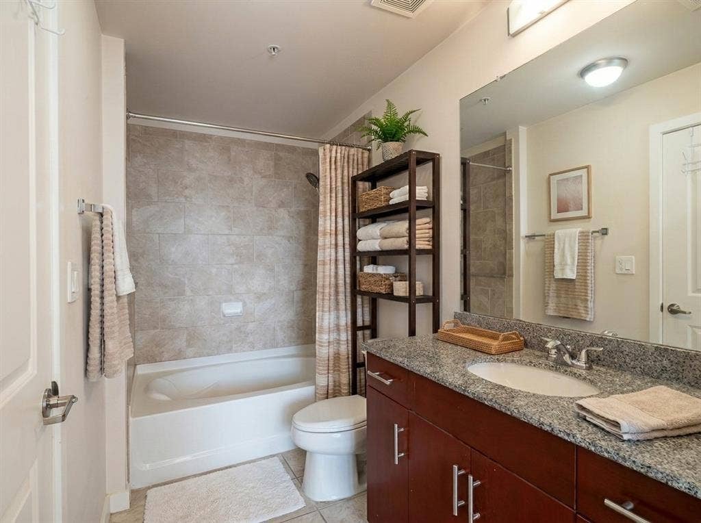 360 Nueces Street, #2110, Austin, TX 78701 Bathroom featuring a built-in bathtub with subway tile surround, granite countertop vanity, wood-finish cabinetry, and recessed lighting Virtually Staged