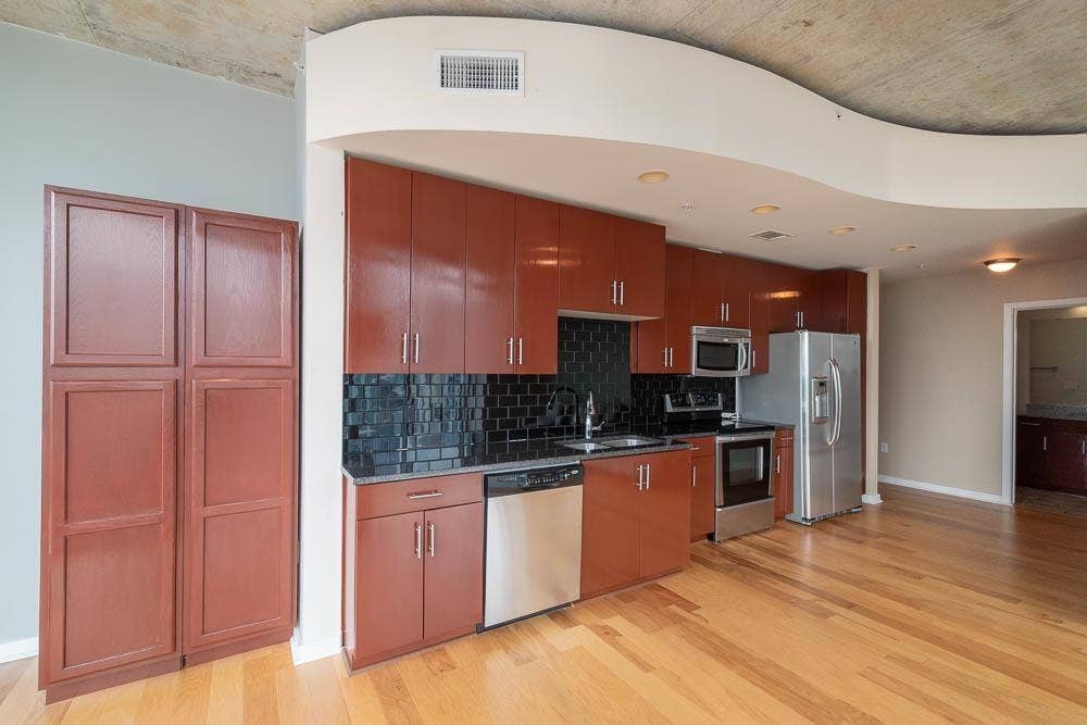 360 Nueces Street, #2110, Austin, TX 78701 Kitchen featuring finish flooring, dark subway tile backsplash, stainless steel appliances, and abundant cabinetry