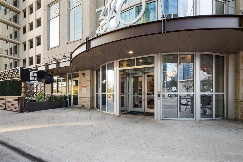 360 Nueces Street, #2110, Austin, TX 78701 Modern commercial building entrance with a curved awning, full-height glass doors, and an integrated exterior dining area