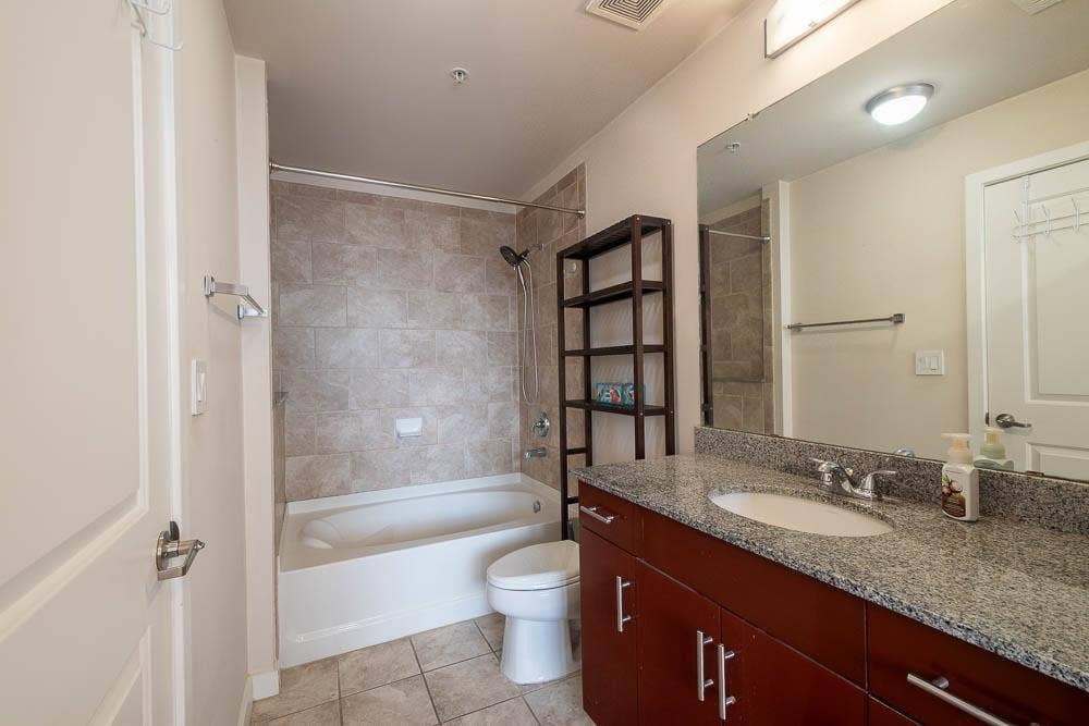 360 Nueces Street, #2110, Austin, TX 78701 Bathroom featuring a granite countertop vanity with an undermount sink, cherry wood-finish cabinetry, and a full bathtub with subway tile surround