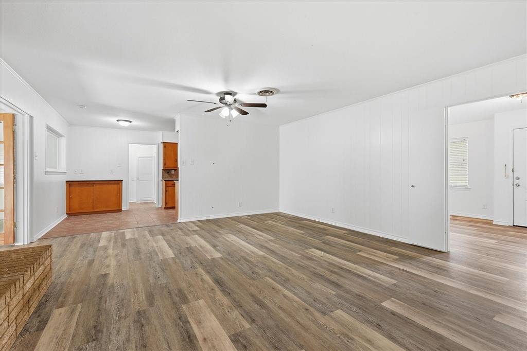 Living area featuring wood-finish flooring, white vertical plank wall paneling, and a ceiling fan