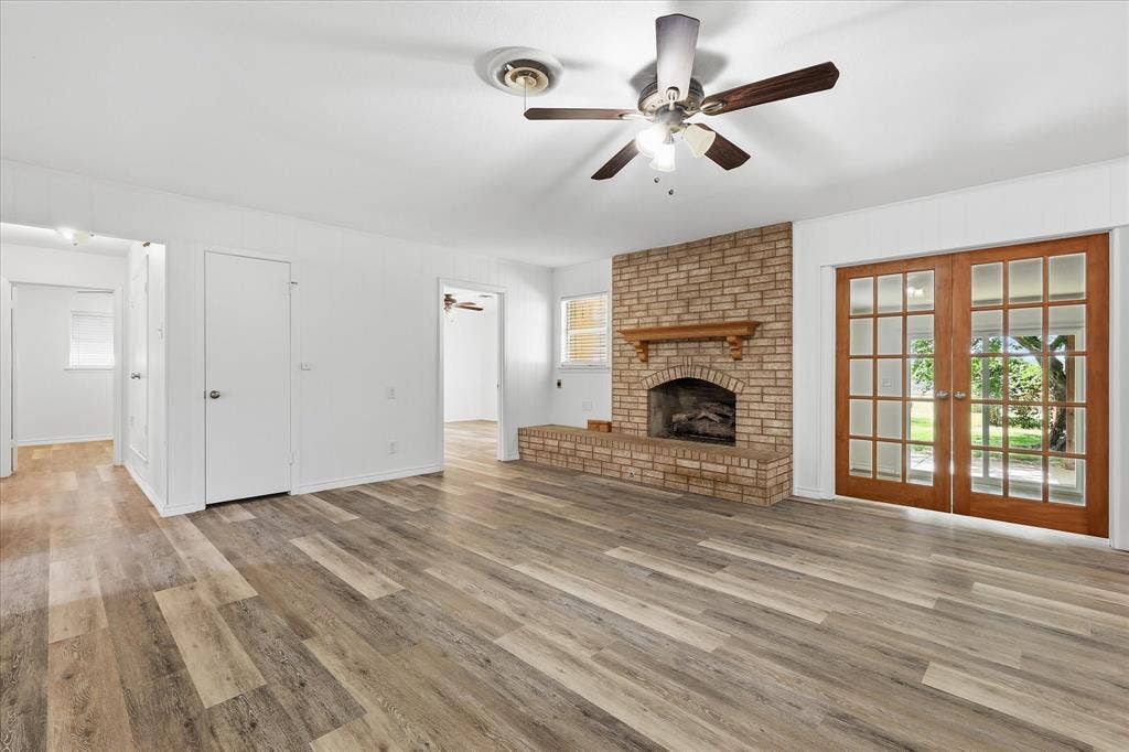 Expansive living area featuring wood-finish flooring, a brick fireplace with a wood mantel, and French doors