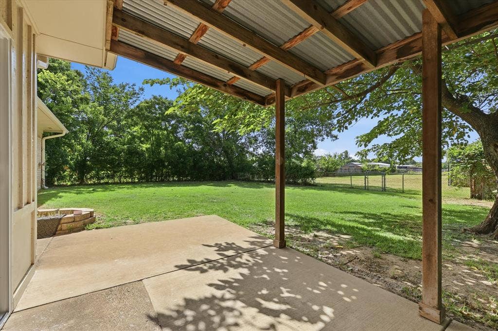 Covered patio featuring a corrugated metal roof supported by wood beams, a concrete slab, and a stone-lined planter