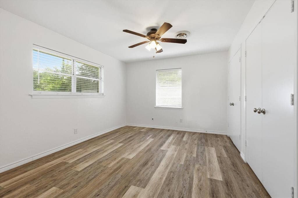 Bright room featuring wood-finish flooring, white walls, and a ceiling fan with integrated lighting