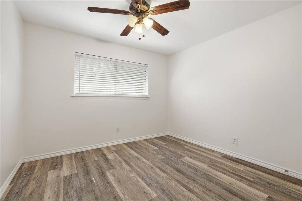 Spacious interior room featuring wood-finish flooring, a window with blinds, and a ceiling fan with light fixture