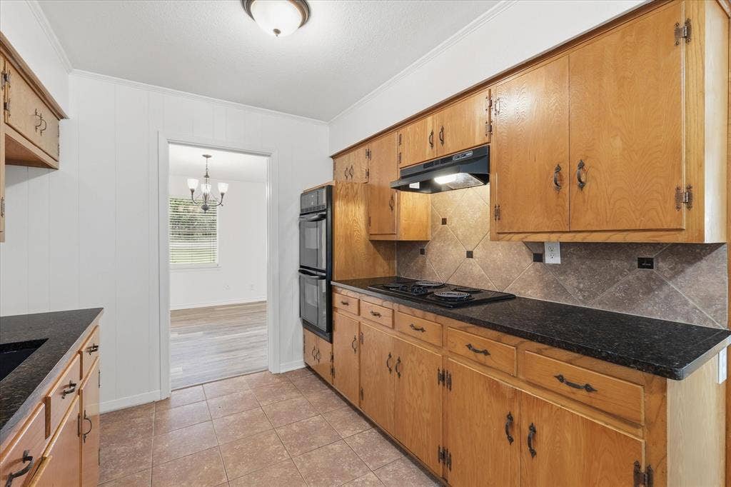 Kitchen featuring natural wood cabinetry, black countertops, and a tiled backsplash
