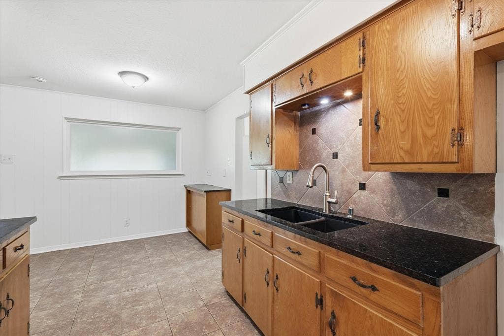 Kitchen featuring wood cabinetry, black countertops, a tile backsplash with diamond-set accents, and a double basin sink with a gooseneck faucet