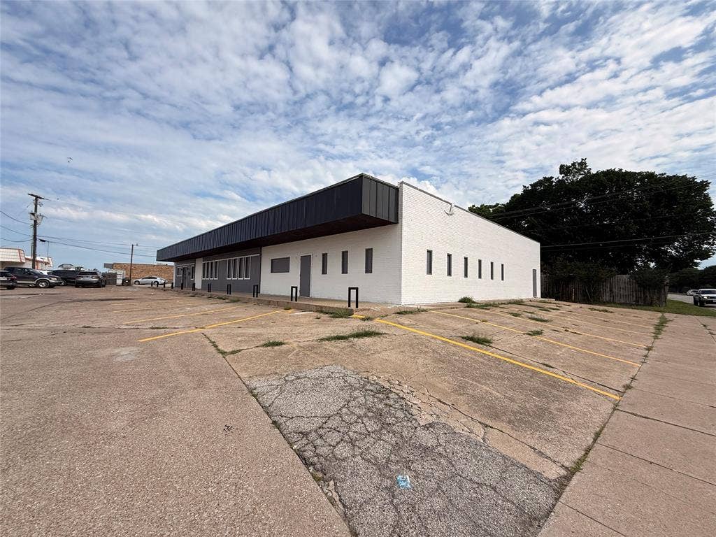 612 Michael Drive, Everman, TX 76140 Commercial building featuring a white brick exterior with dark trim and a substantial parking area