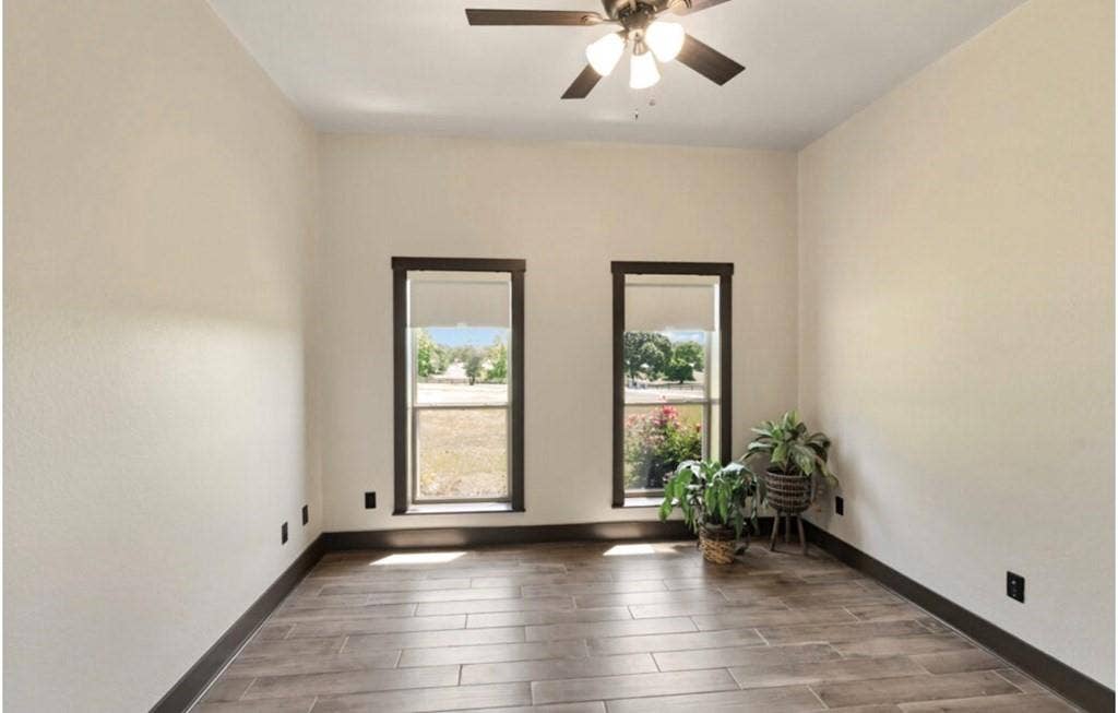 106 Timber Hill, Athens, TX 75751 Room featuring wood-look tile flooring, two windows with dark trim, a ceiling fan with integrated lighting, and neutral wall paint