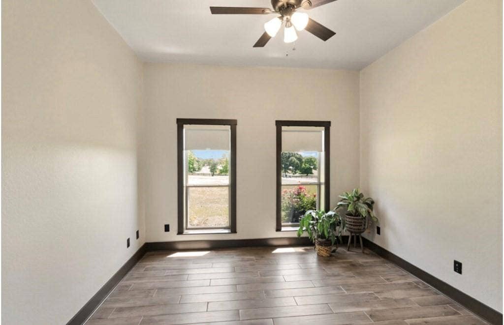 106 Timber Hill, Athens, TX 75751 Room featuring two tall windows with dark trim, wood-finish flooring, a ceiling fan with integrated lighting, and neutral-toned walls