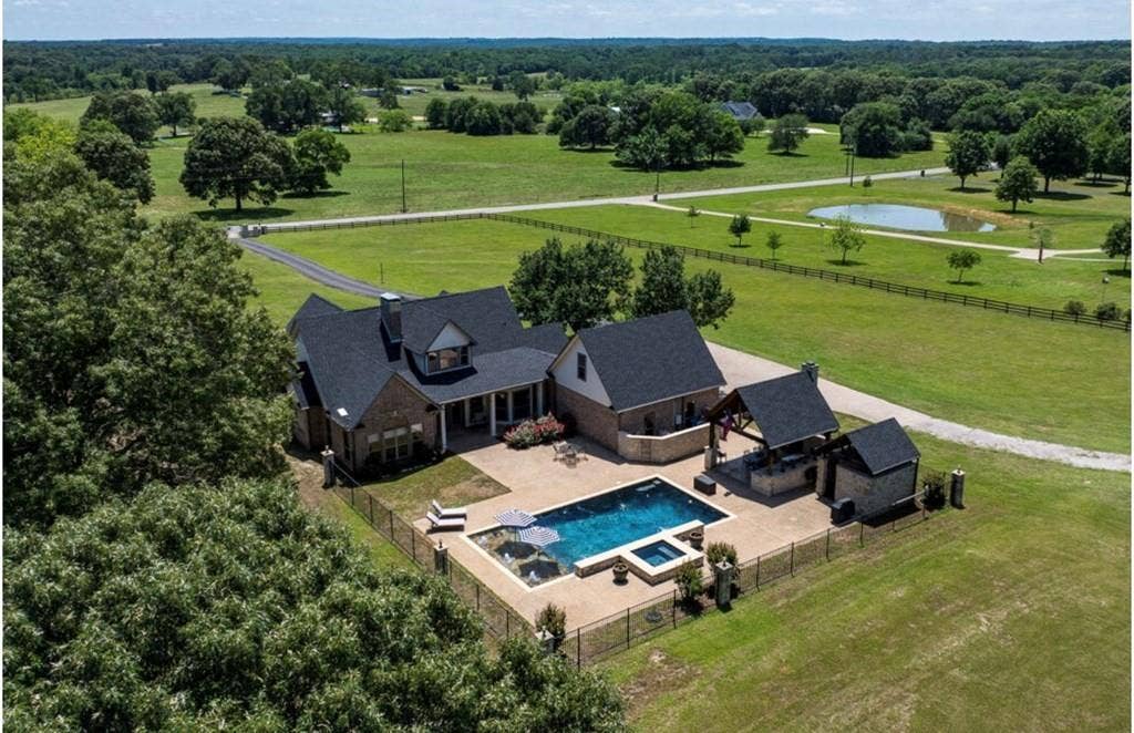 106 Timber Hill, Athens, TX 75751 Expansive brick residence featuring a large patio, fenced swimming pool with integrated spa, and an outdoor kitchen area with a covered pergola