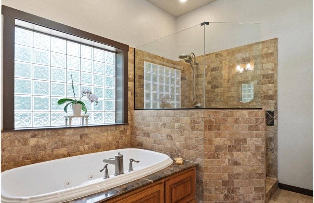 106 Timber Hill, Athens, TX 75751 Bathroom featuring a built-in jetted tub with polished chrome fixtures, a wood-finish vanity, and a glass block window