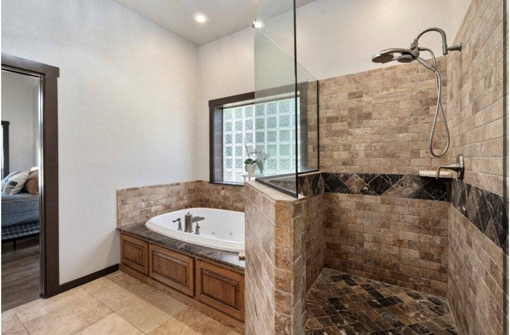 106 Timber Hill, Athens, TX 75751 Expansive bathroom featuring a walk-in shower with stone-finish tile, a built-in jetted tub with wood-finish cabinetry, a glass block window, and recessed lighting