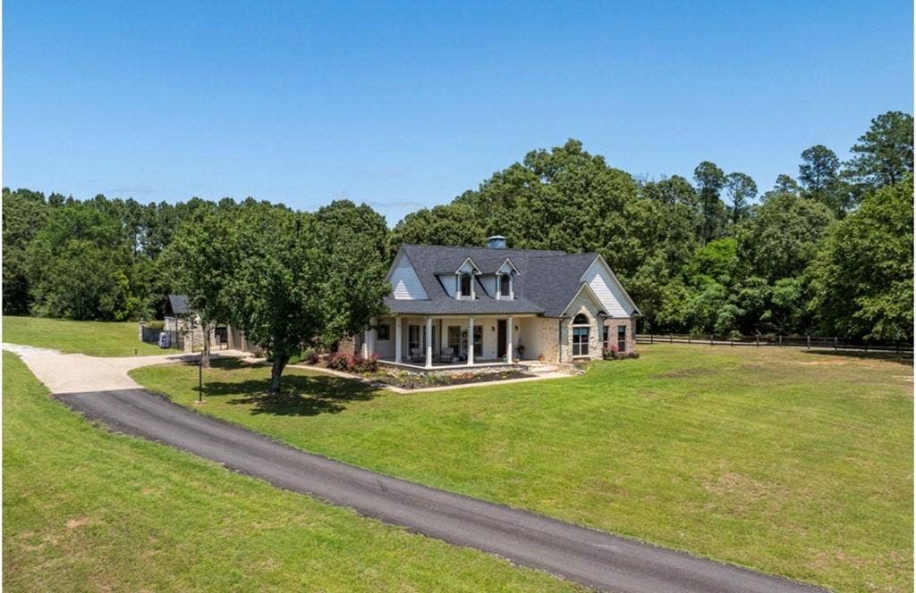 106 Timber Hill, Athens, TX 75751 Stone and siding exterior featuring a dark shingle roof with dormer windows, a covered front porch, an arched window, and a paved driveway