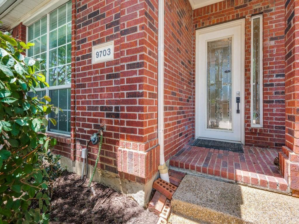 9703 Raven Lane, Irving, TX 75063 Brick exterior featuring a white entry door with decorative glass, two sidelight windows, and a grid-pane window
