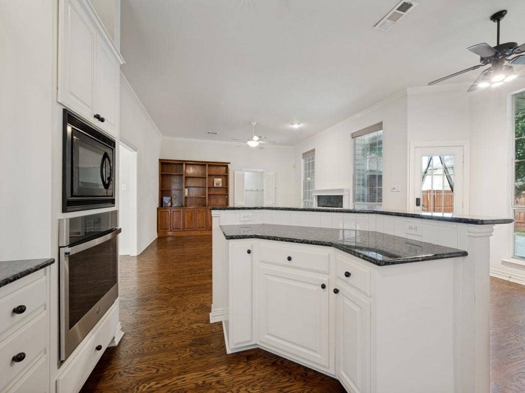 9703 Raven Lane, Irving, TX 75063 Spacious kitchen featuring white cabinetry, dark stone countertops, built-in stainless steel appliances, and a breakfast bar