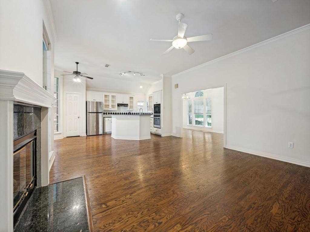 9703 Raven Lane, Irving, TX 75063 Open concept living area featuring wood-finish flooring, a fireplace with a stone surround and hearth, white walls, and crown molding