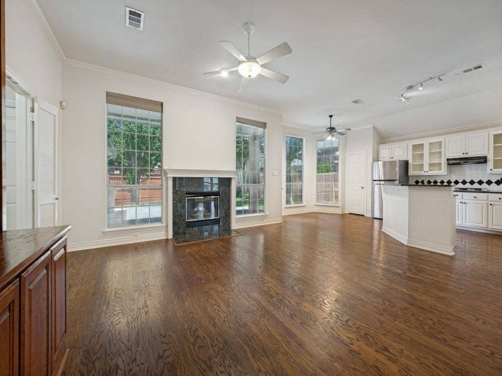 9703 Raven Lane, Irving, TX 75063 Open-concept living area featuring rich wood-finish flooring, a fireplace with a dark stone surround, multiple large windows, and an integrated kitchen with white cabinetry and stainless steel appliances